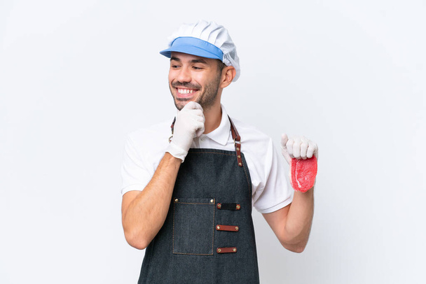 Butcher caucasian man wearing an apron and serving fresh cut meat over isolated white background looking to the side and smiling - Photo, Image