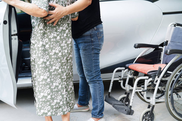 Опекун помочь азиатской пожилой женщины инвалидности пациент сесть в машину, медицинская концепция. - Фото, изображение