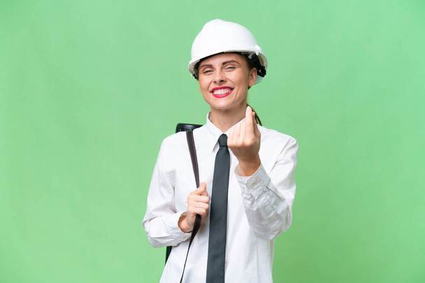 Young architect woman with helmet and holding blueprints over isolated background making money gesture - Photo, Image