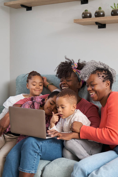 自宅のラップトップの前で楽しい時間を過ごしている幸せなアフリカの水平方向の拡張家族. - 写真・画像
