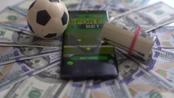 Концепция футбольного бизнеса. Мяч и смартфон с приложением ставки на долларовые купюры и зеленый фон. Концепция игры в футбол на деньги. Высокое качество фото - Кадры, видео