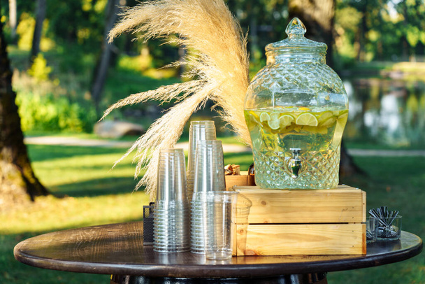 Limonadi lasissa koristeellinen juoma-annostelija, kertaluonteiset lasit pöydällä puutarhajuhlissa. - Valokuva, kuva