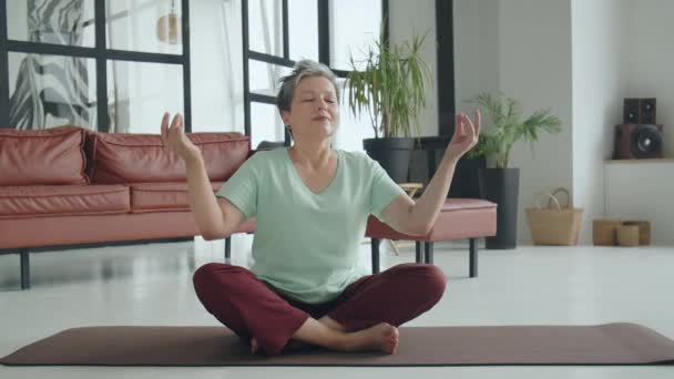 Стара жінка робить вправи на йогу вдома. Зріла жінка має медитацію. Вона закриває очі і намагається знайти внутрішню концентрацію. щасливе старе життя. Високоякісні 4k кадри - Кадри, відео
