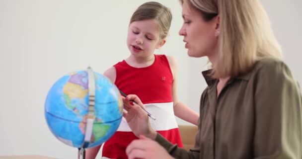 Neugierige kleine Mädchen und eine positive Frau blicken auf den Globus am Tisch. Studentin erkundet Weltkarte mit Mutter im Licht. Lektion in Geografie-Zeitlupe - Filmmaterial, Video