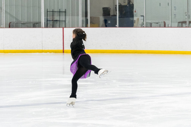Artistik patinaj rutinini mükemmelleştiren genç bir kız kapalı bir buz pateni sahasında yarışma elbisesini giyerken. - Fotoğraf, Görsel
