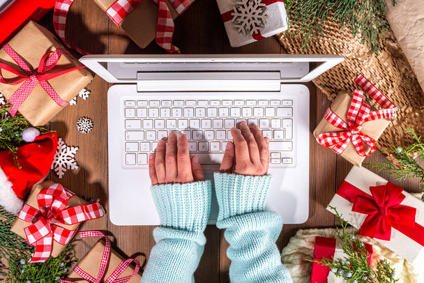 Personne utilisant un ordinateur portable avec des boîtes-cadeaux de Noël d'en haut sur fond en bois. Carnet avec mains de femme avec cadeaux, sapin et décor d'hiver. Préparation pour Noël, Nouvel An - Photo, image