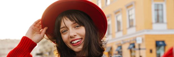 close-up van een glimlachende jonge stijlvolle brunette witte vrouw dragen hoed en leren jas met kort haar staan op een straat het nemen van selfie - Foto, afbeelding