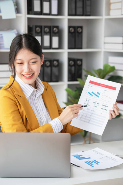 Ázsiai üzletasszony munkavállaló vagy menedzser sárga öltönyben jó hangulatban egy laptop és számológép segítségével kiszámítja a vállalati jövedelem és ráfordítások egyenlege az irodában. - Fotó, kép