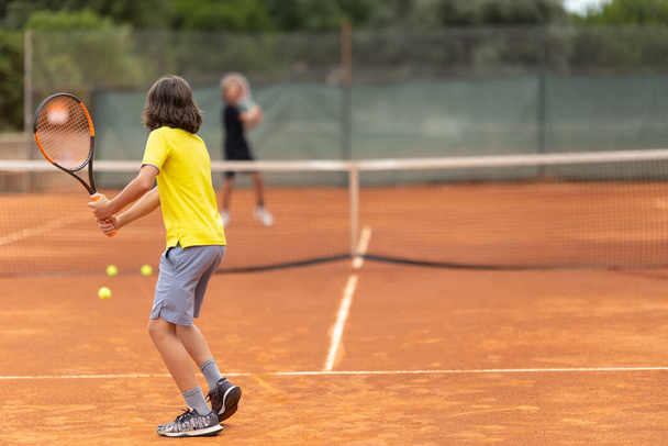Two boys playing friendly tennis match on the court. Mid shot - Photo, Image