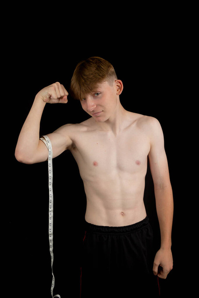 Portrait of a sporty shirtless teenage boy measuring his bicep - Photo, image