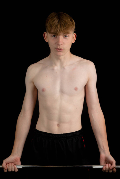 Portrait of a sporty shirtless teenage boy exercising with a barbell - Fotó, kép