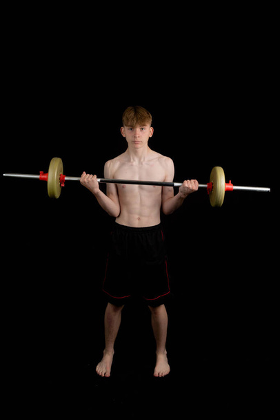 Portrait of a sporty shirtless teenage boy exercising with a barbell - Фото, зображення