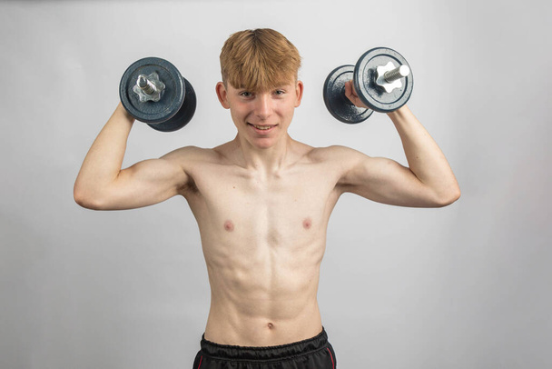 Portrait of a sporty shirtless teenage boy exercising with dumbbells - Fotó, kép