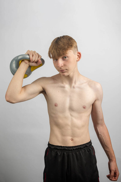 Portrait of a sporty shirtless teenage boy lifting a kettlebell - Foto, afbeelding
