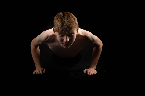 Portrait of a sporty shirtless teenage boy doing press ups from the front - Фото, зображення