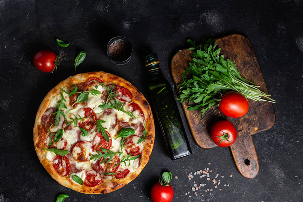 Pizza met ham, tomaten en mozzarella op een donkere achtergrond - Foto, afbeelding