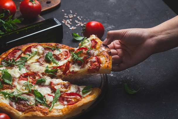 Pizza com presunto, tomate e mussarela sobre um fundo escuro - Foto, Imagem