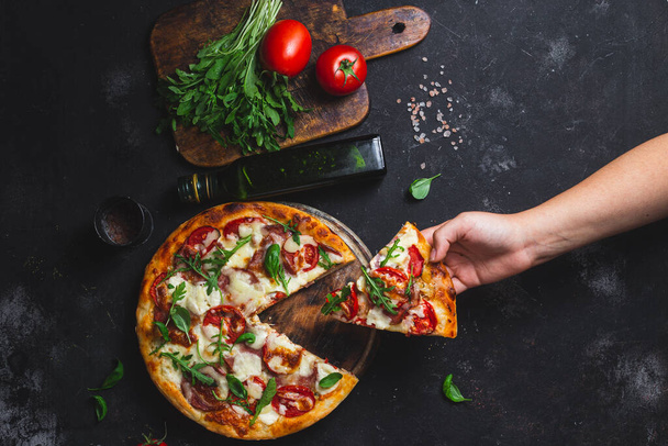 Pizza met ham, tomaten en mozzarella op een donkere achtergrond - Foto, afbeelding