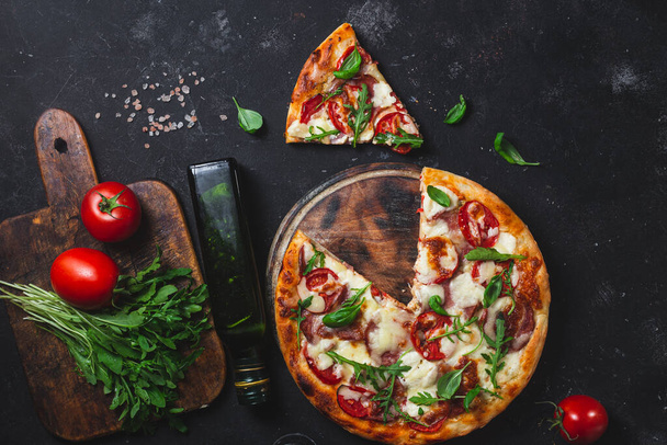 Pizza con jamón, tomate y mozzarella sobre fondo oscuro - Foto, Imagen