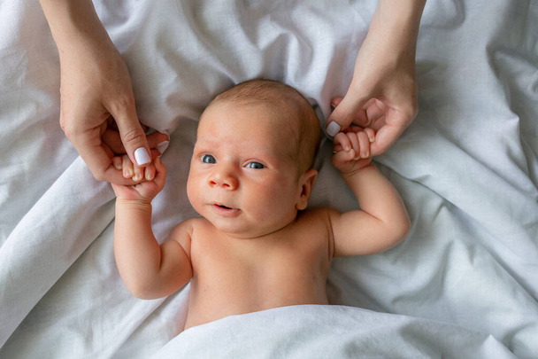 Schattig klein jongetje in een kinderbedje, mama 's handen vasthoudend, klaar om wakker te worden. Bovenaanzicht van schattige peuter wakker worden, liggen in bed, grijpen moeder vingers - Foto, afbeelding