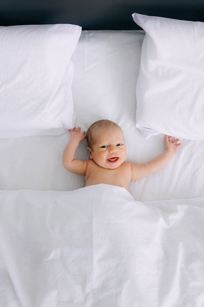 カメラを見ているベッドに横たわる白い赤ん坊の少年を笑うかわいい愛らしい笑顔の肖像画. 上からの眺め. 幸せな子供時代のライフスタイル. - 写真・画像