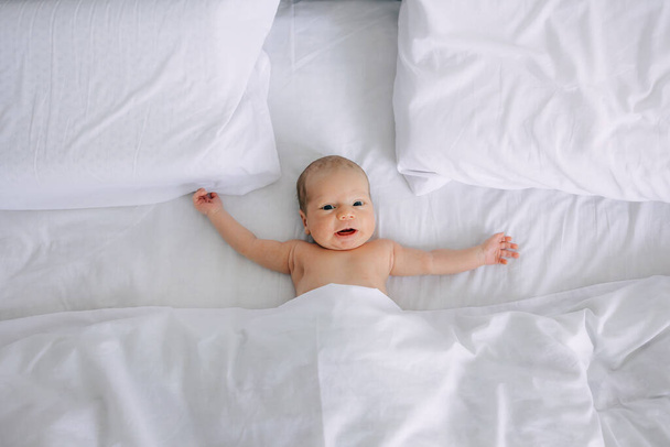 ベッドの上に横たわる愛らしい赤ちゃんのトップビュー,好奇心を持ってカメラを見る. - 写真・画像