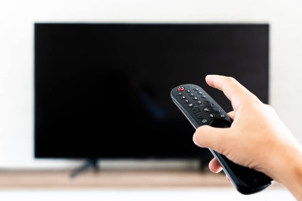 Рука тримає пульт дистанційного керування для вимкнення телевізора. порожній чорний екран телевізора. - Фото, зображення