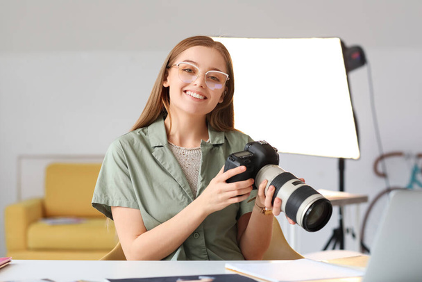 スタジオのテーブルでプロのカメラを持つ若い女性写真家 - 写真・画像