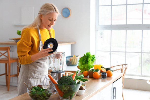 Зрелая женщина с блендером делает здоровый смузи на кухне - Фото, изображение