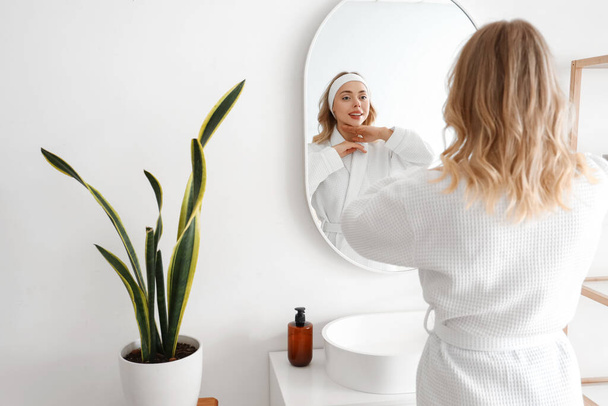 Young woman doing face building exercise near mirror in bathroom - Fotó, kép