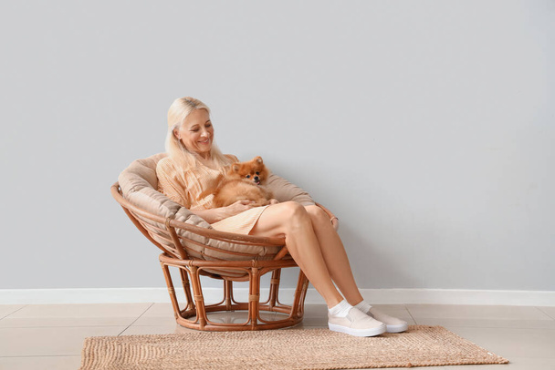 Mature woman with Pomeranian dog in armchair near light wall - Foto, afbeelding