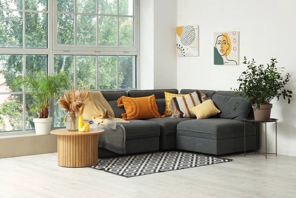 Interieur van lichte woonkamer met gezellige grijze bank, salontafel en kamerplanten - Foto, afbeelding