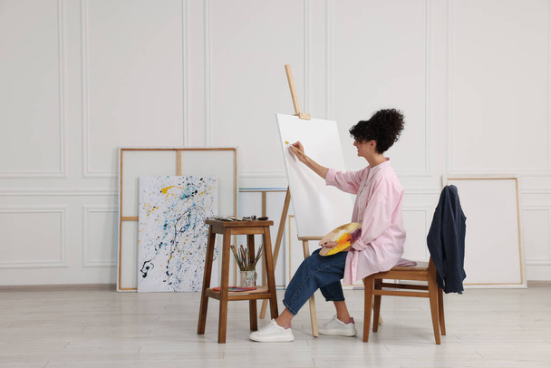 Young woman painting on easel with canvas in studio - Photo, Image