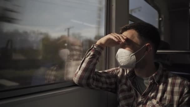 Cansado deprimido viajero masculino con máscara protectora contra la infección por Coronavirus está sentado dentro del tren y mirando por la ventana. Nueva Normal. Distancia social al viajar en transporte público.  - Metraje, vídeo