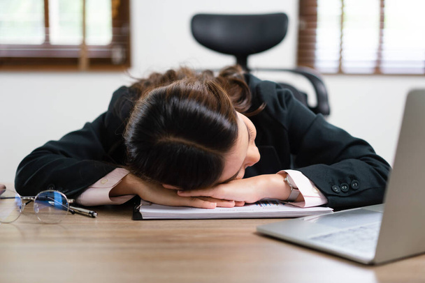 Femme d'affaires dormant sur son bureau près d'un ordinateur portable après avoir été épuisée par le surmenage sur le lieu de travail. - Photo, image