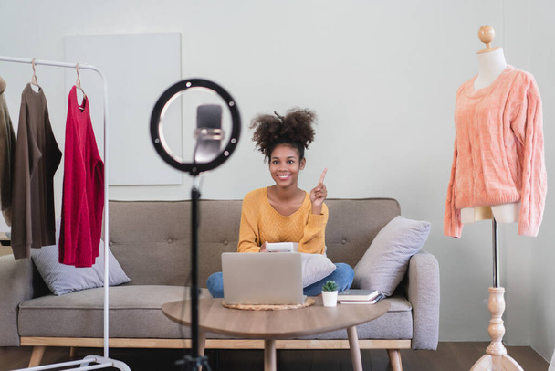 La femme commerçante de mode afro-américaine utilise son smartphone pour vendre des vêtements en direct en streaming. - Photo, image