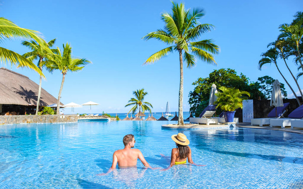 Man and Woman relaxing in a swimming pool, a couple on a honeymoon vacation in Mauritius tanning in the pool with palm trees and sun beds - Photo, Image