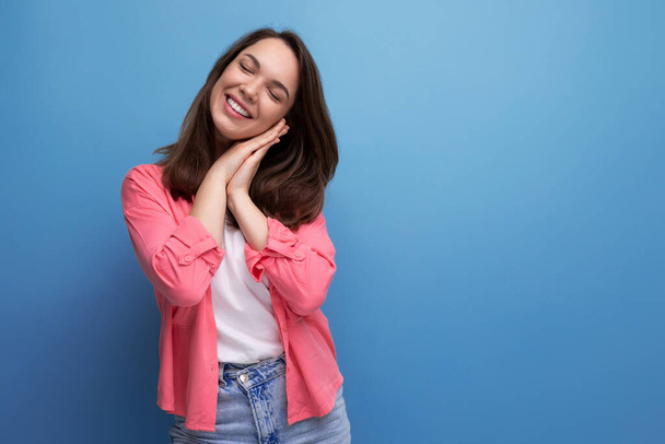 γοητευτική χαμογελαστή μελαχρινή νεαρή γυναίκα με ροζ πουκάμισο και τζιν σε ένα στούντιο απομονωμένο φόντο. - Φωτογραφία, εικόνα