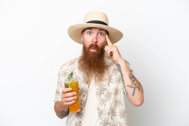 Uomo dai capelli rossi con lunga barba che beve un cocktail su una spiaggia isolata su sfondo bianco pensando a un'idea - Foto, immagini