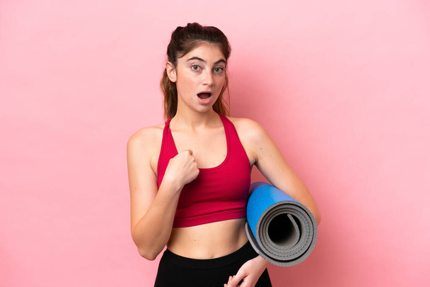 Молода спортивна жінка ходить на заняття з йоги, проводячи мат з несподіваним виразом обличчя
 - Фото, зображення