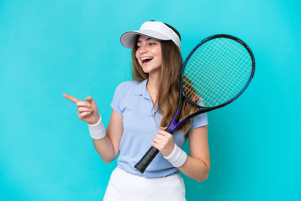 Junge Tennisspielerin isoliert auf blauem Hintergrund zeigt mit dem Finger zur Seite und präsentiert ein Produkt - Foto, Bild