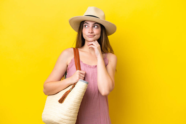 Jonge blanke vrouw met een strandtas geïsoleerd op gele achtergrond met twijfels en denken - Foto, afbeelding