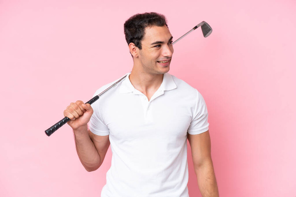 Fiatal golfozó játékos férfi elszigetelt rózsaszín háttér néz oldalra, és mosolygós - Fotó, kép