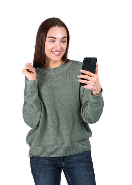 Young woman portrait with a happy smile, looking at smartphone in hand. Isolated over white background. Concept of online communication and social media - Photo, Image