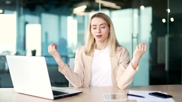 Young woman is meditating with her eyes closed while sitting at a workplace in the office. Businesswoman took a break from work to relieve stress. Female employee rests, relaxes, feels peace of mind - Filmagem, Vídeo
