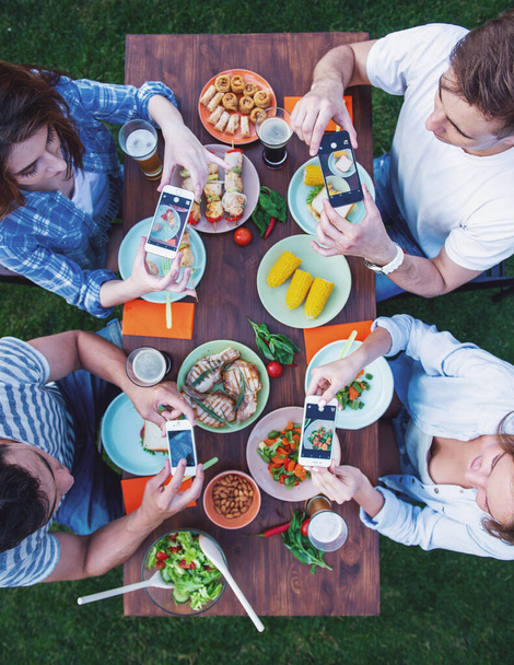 A fiatal, szép emberek fotózni az élelmiszer, miközben az asztalnál ül, és miután piknik a szabadban felülnézet - Fotó, kép