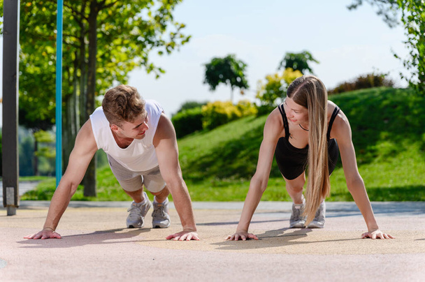Young pretty couple doing push-ups on the outdoor sports ground in the city park. - Photo, Image