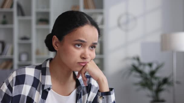 Attractive African American girl sitting in living room, resting hand on cheek, looking tired. Sad young girl suffers from negative thoughts, has depression relationship problems, regrets mistakes - Filmmaterial, Video