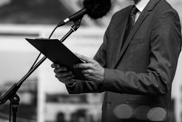 Orador masculino em um palco vestindo terno na conferência de imprensa ao ar livre. - Foto, Imagem