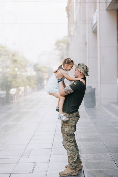Μικρή Ουκρανή συναντά τον πατέρα της από τον πόλεμο κατά τη διάρκεια των διακοπών του και χαρούμενη τον αγκαλιάζει. Πόλεμος στην Ουκρανία. Ρωσική στρατιωτική εισβολή στην Ουκρανία. Πόλεμος και παιδιά. - Φωτογραφία, εικόνα